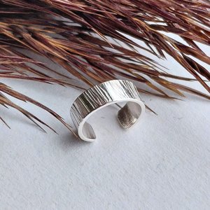 Sterling silver ear cuff with hammered texture photographed from another angle on natural dried grasses