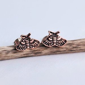 Pair of copper moth stud earrings displayed side by side on natural wood