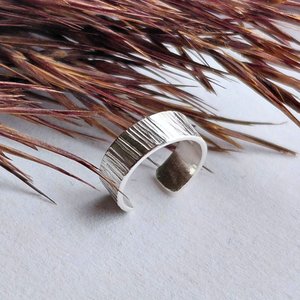 Handmade sterling silver ear cuff with textured surface shown against natural dried grasses