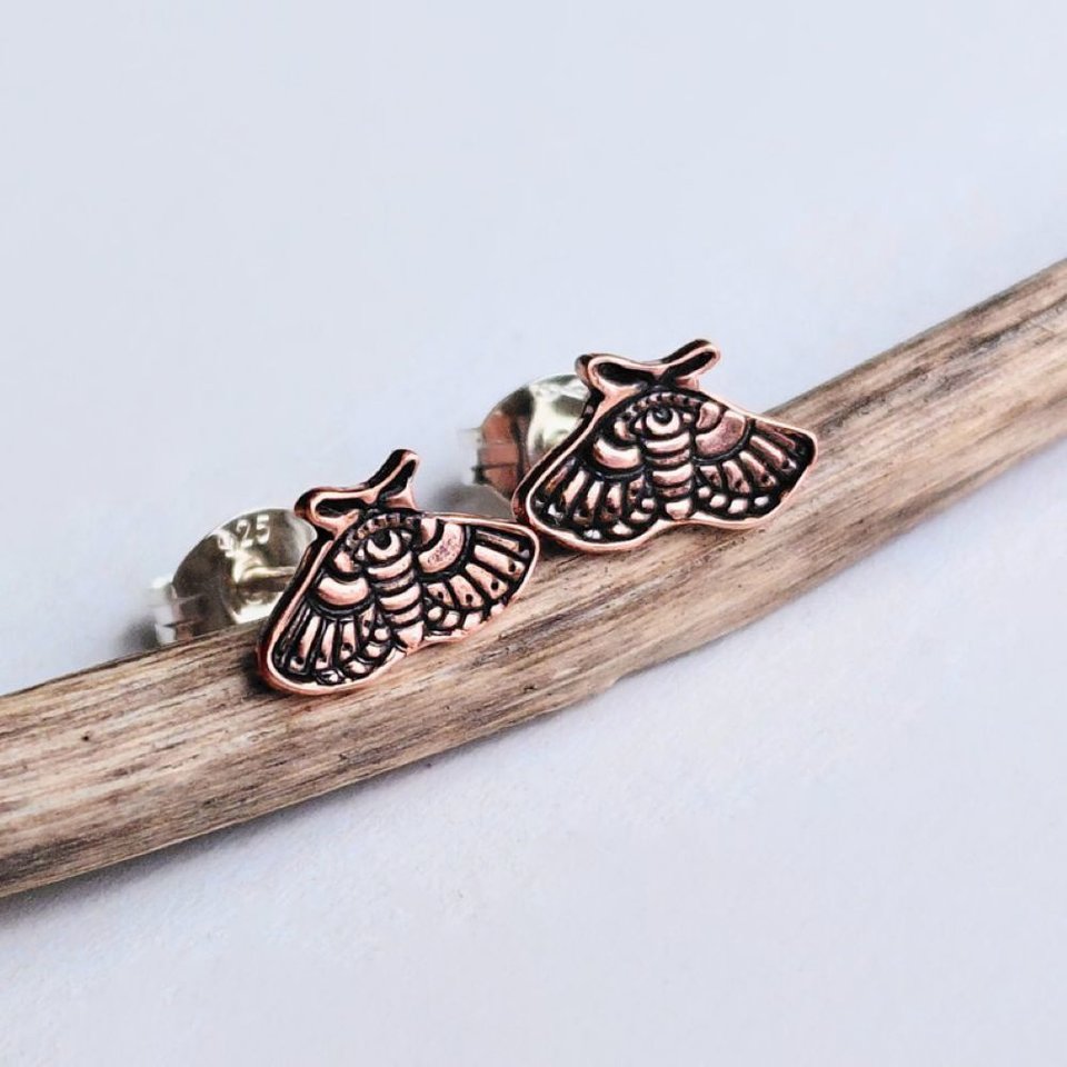 Pair of copper moth stud earrings with intricate moth detailing on a rustic wood surface