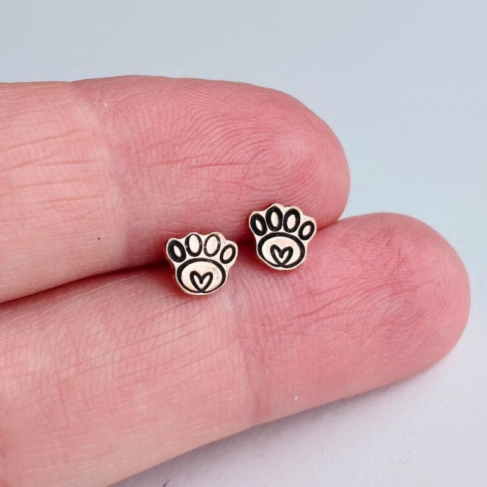 Small copper paw print stud earrings held between fingertips to show their size