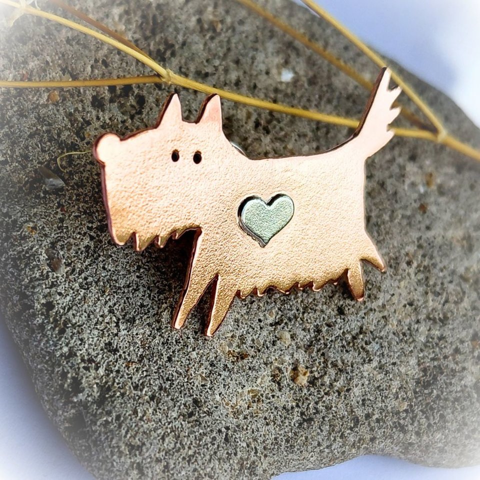 Angled view of the handcrafted copper scruffy terrier dog brooch with a sterling silver heart