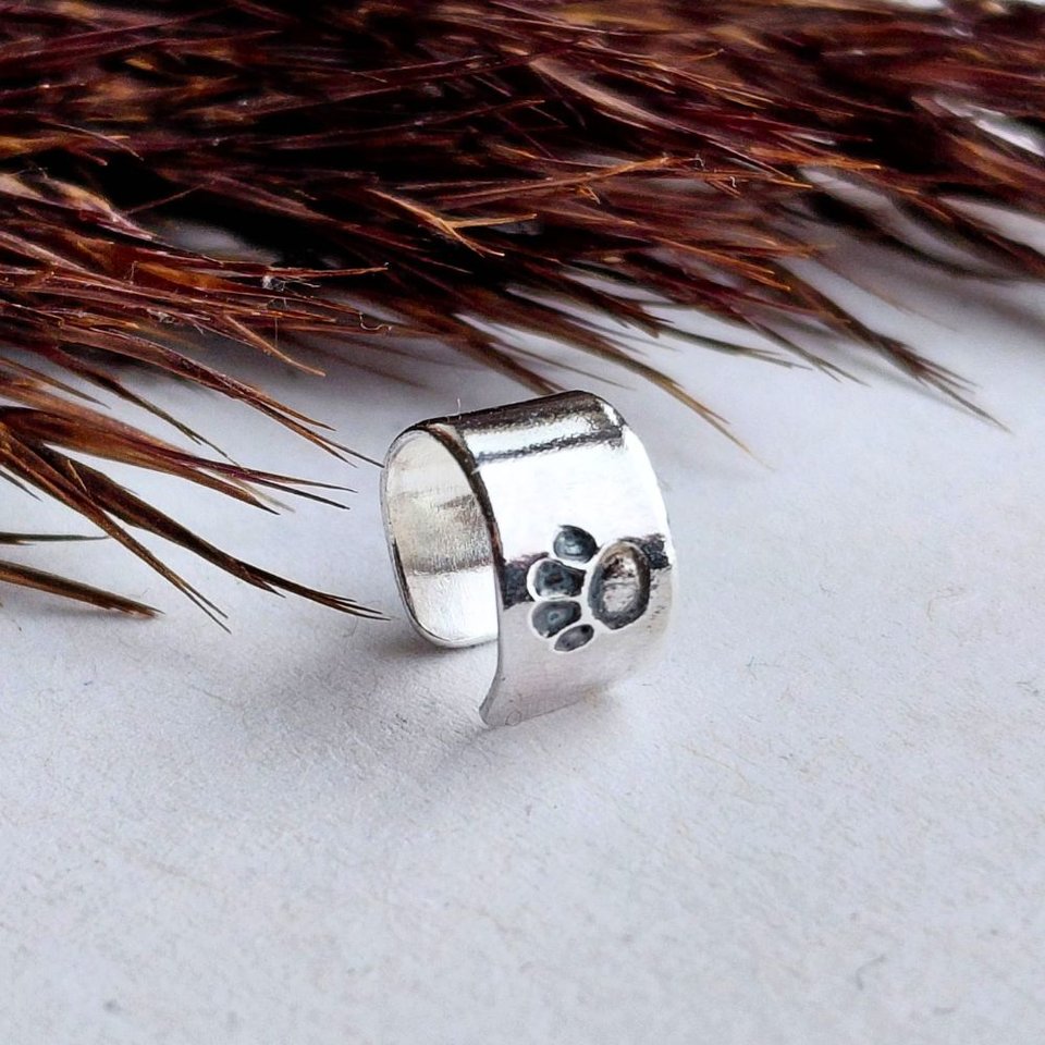 Sterling silver paw print helix cuff shown from a different angle on a white background with dried grasses