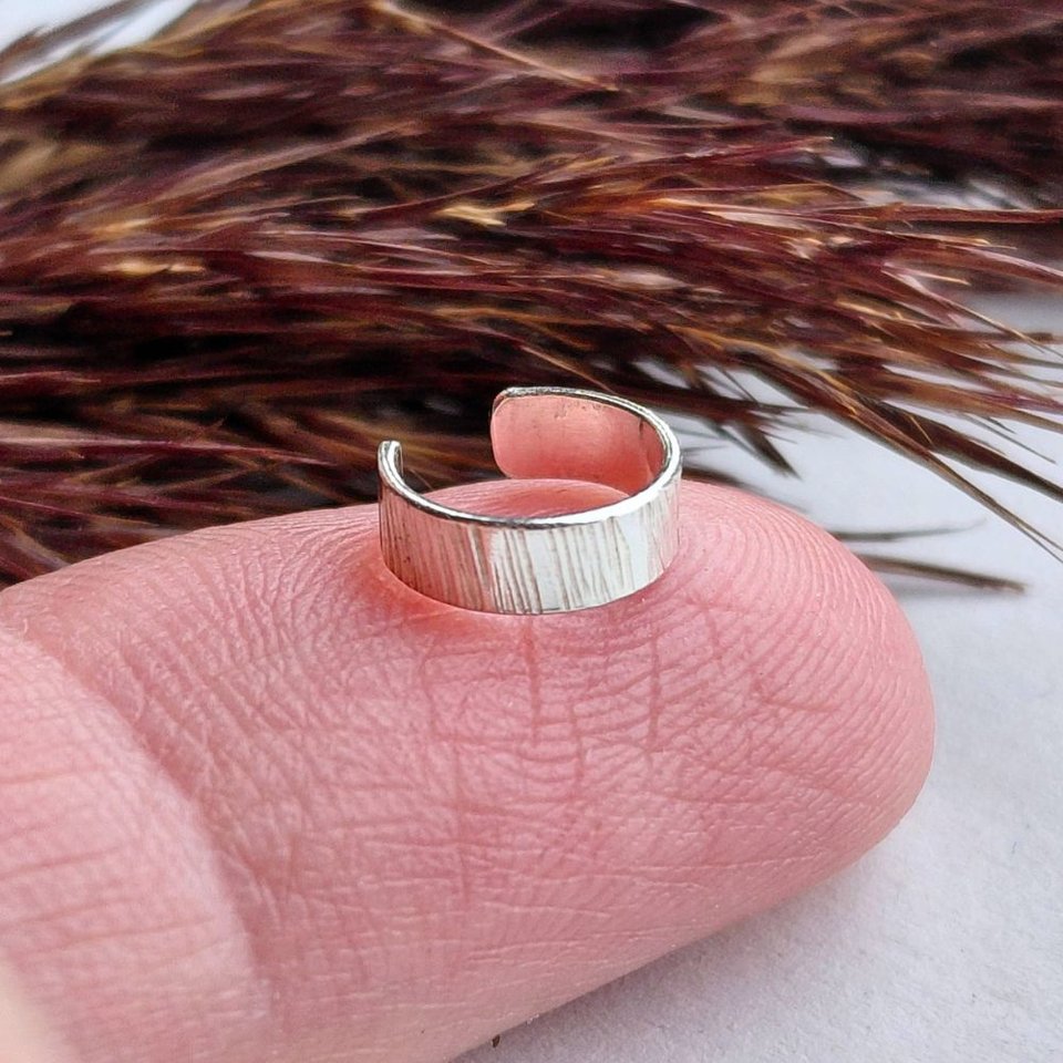 Sterling silver hammered ear cuff shown on a fingertip to demonstrate its size 