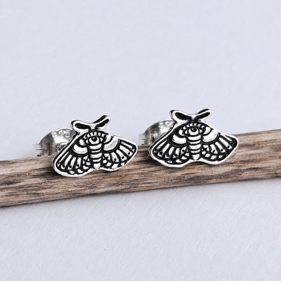 Pair of handmade sterling silver moth stud earrings displayed on natural wood