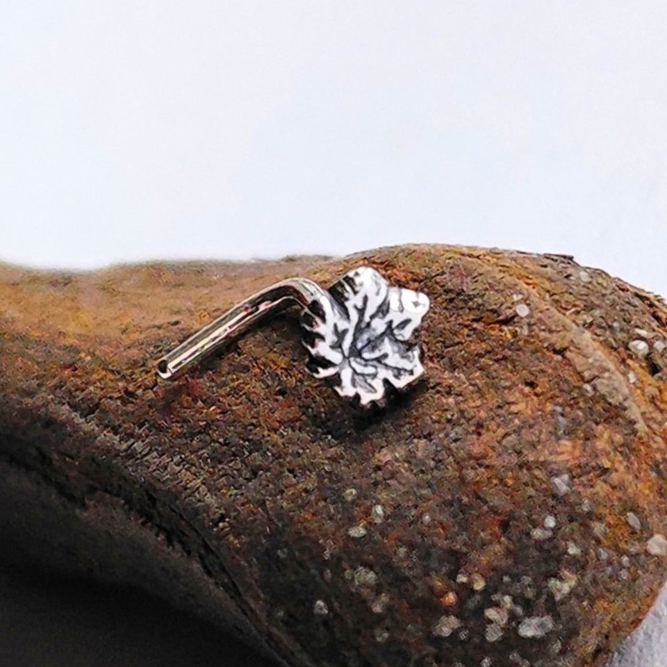 Fine silver maple leaf nose stud with a sterling silver L-shaped post, shown on natural wood